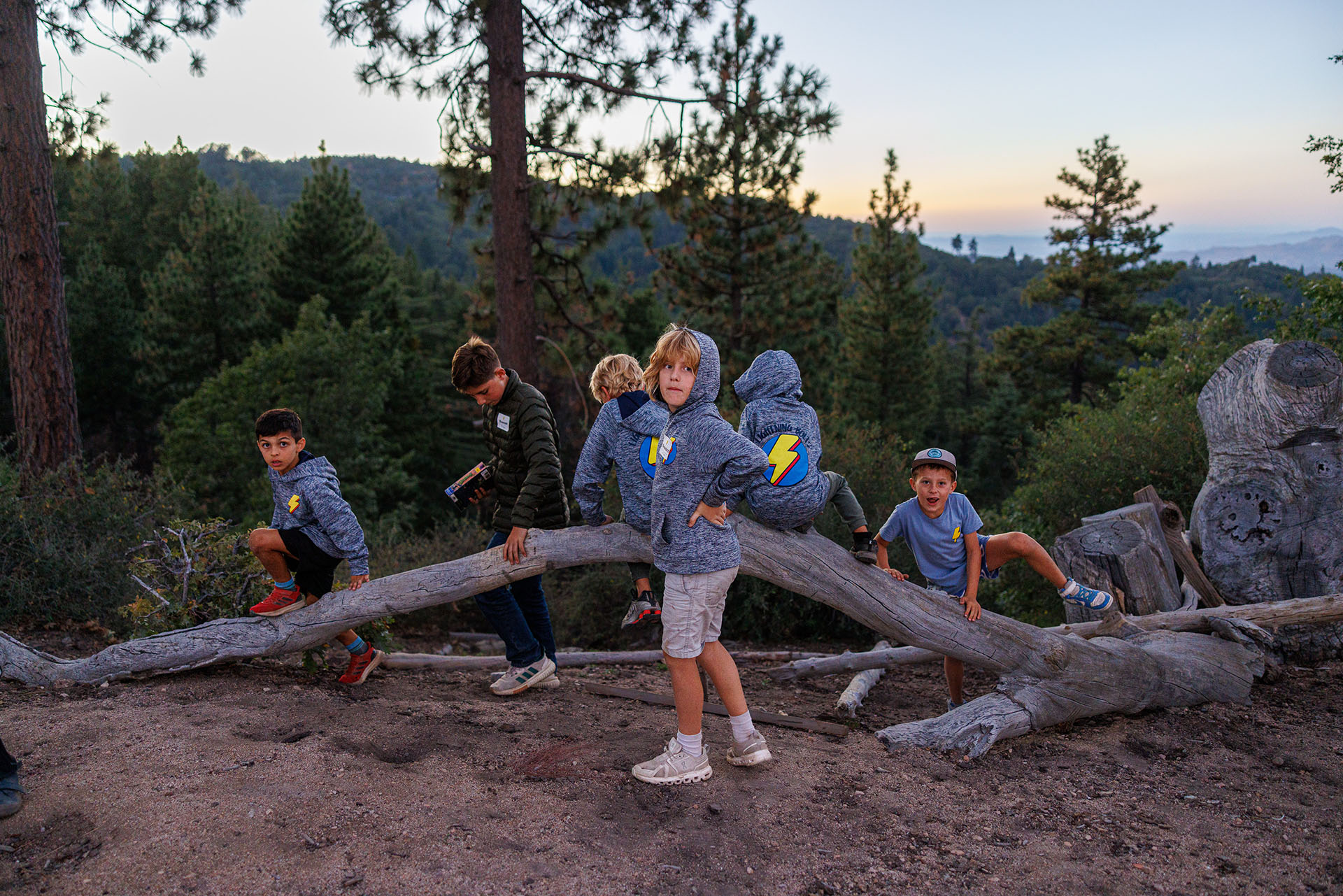 Lightning Bolts boys exploring fallen logs beneath the pine trees at sunset at Pali